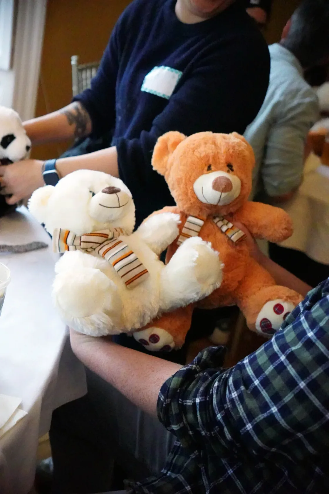 A person holding two teddy bears during an indoor activity.