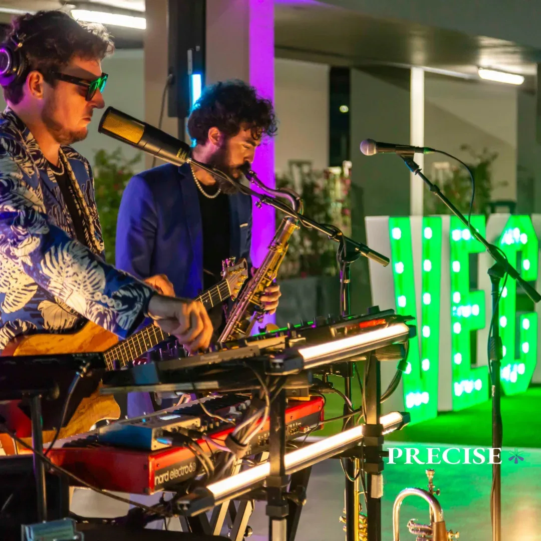 A live band performing beside green illuminated event lettering.
