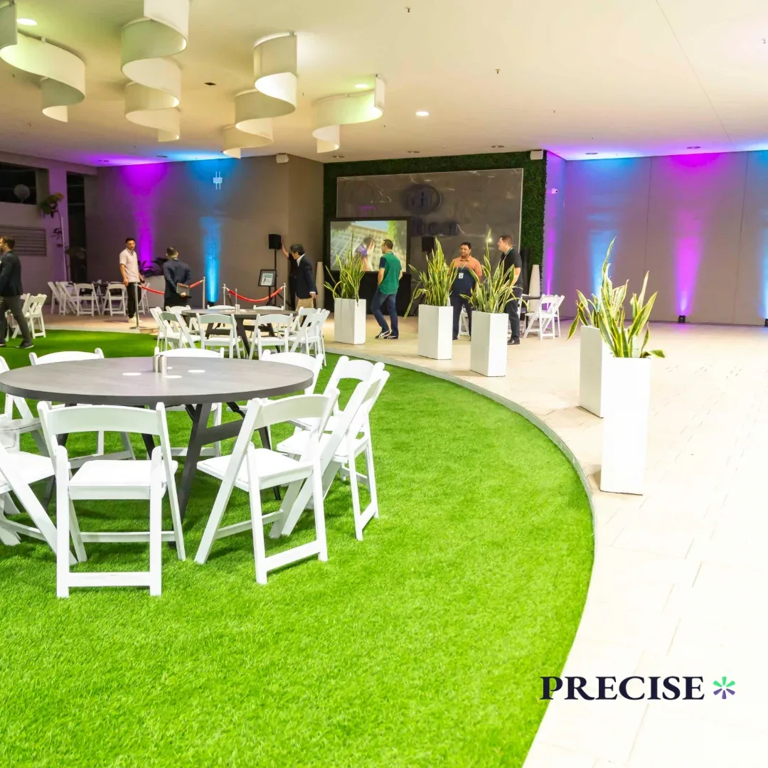 An indoor event space with white furniture, green flooring and purple lighting.