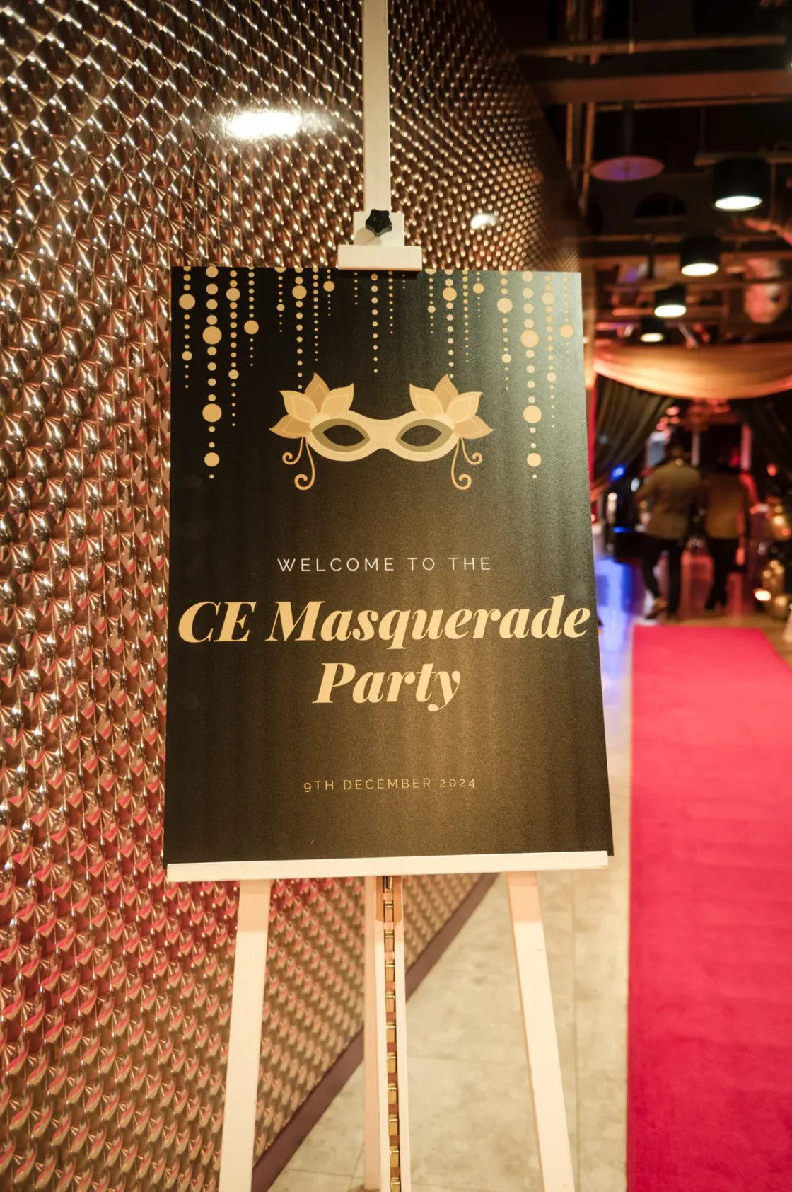 A welcome sign for a masquerade party inside an event venue.