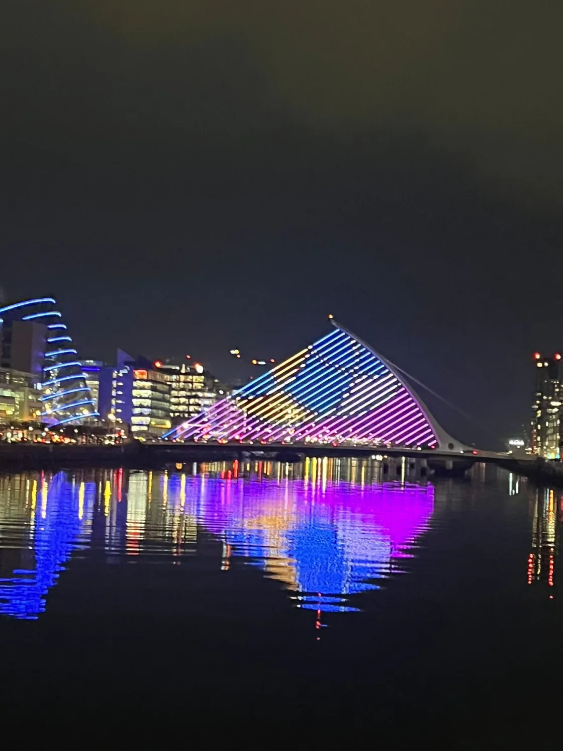 A glass-roofed waterfront building reflected in the water at night.