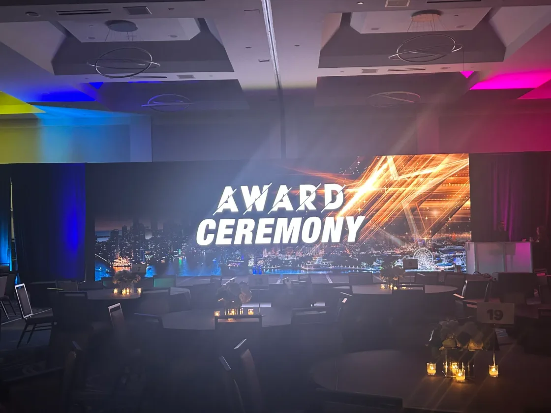 A wide awards-ceremony screen on a stage lit in blue and purple.