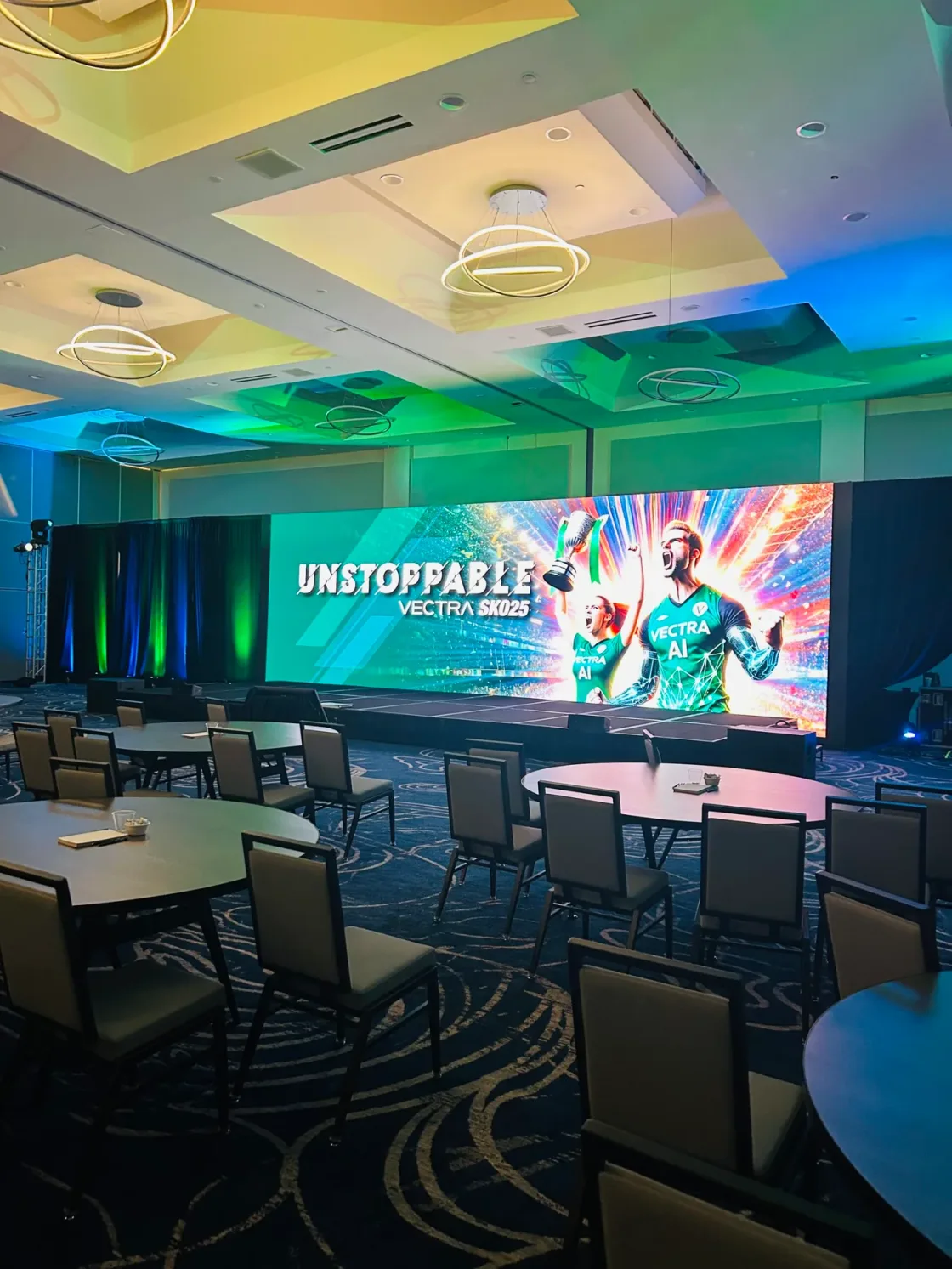 Conference seating and tables arranged in front of a wide presentation screen.