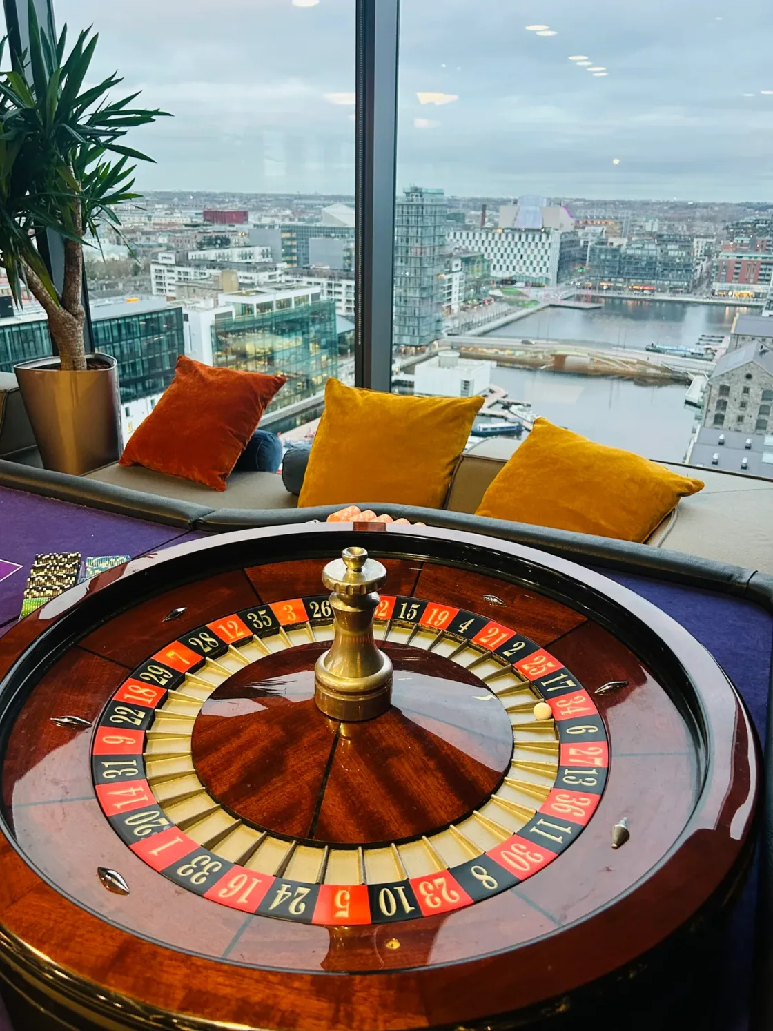 A roulette table beside lounge seating and panoramic windows.