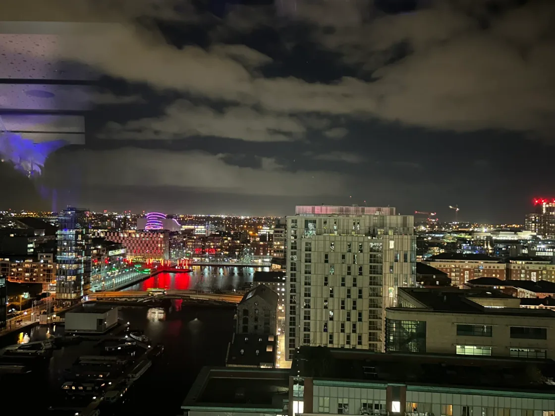 An illuminated city skyline beneath a cloudy night sky.