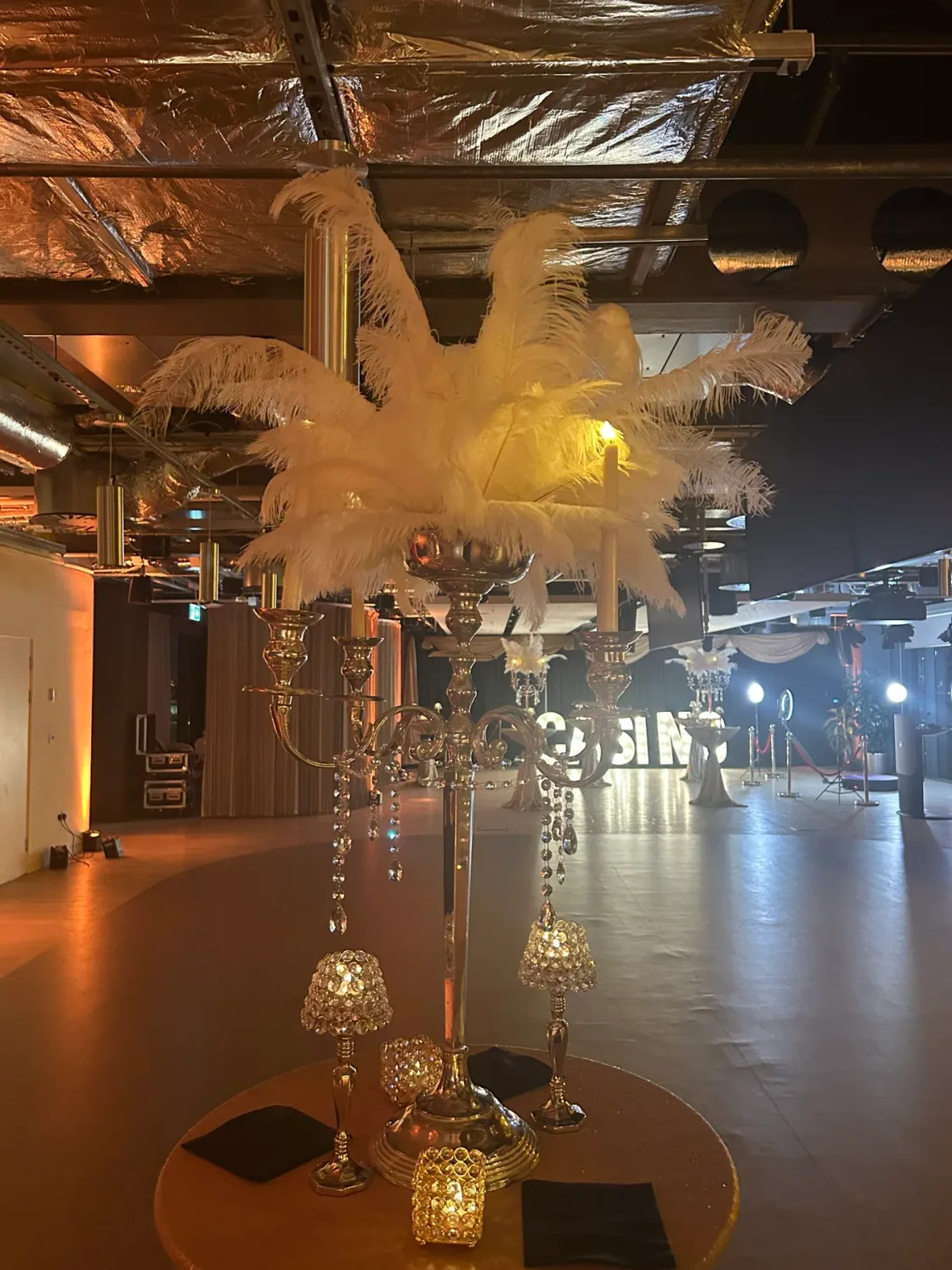A tall feathered table decoration inside a warmly lit event venue.