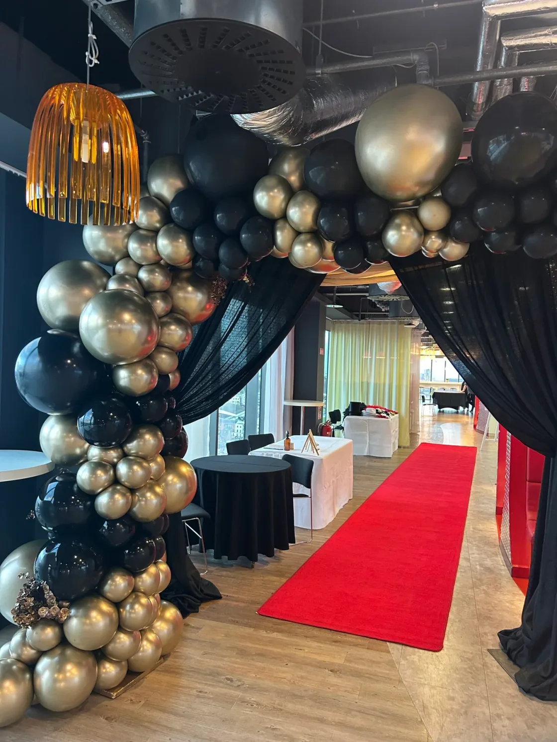 A black-and-gold balloon arch above a red-carpet entrance.