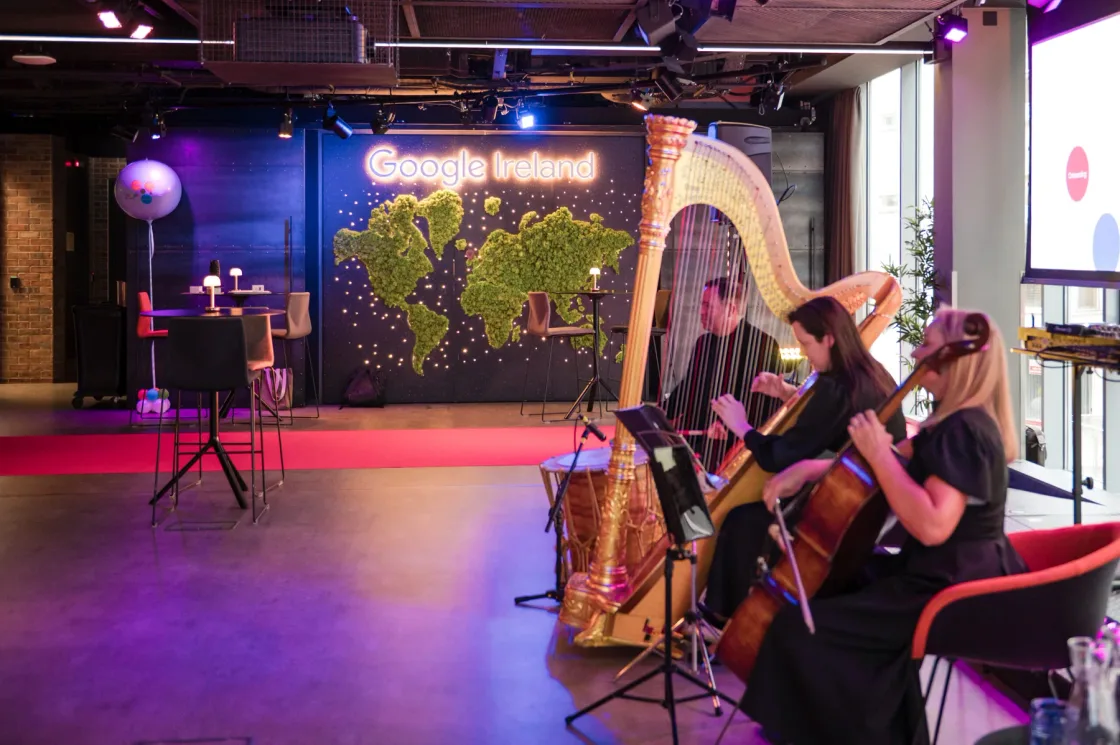 A harpist and cellist beside an illuminated green world-map backdrop at a Dublin event.
