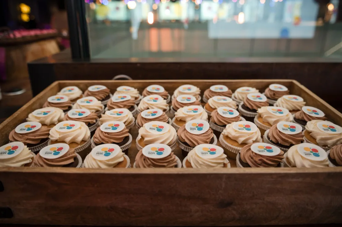 A wooden tray filled with decorated cupcakes.