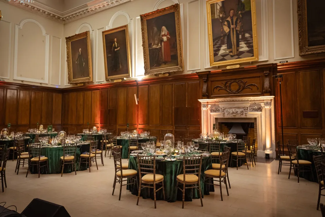 Dining tables prepared in a panelled hall beneath large portrait paintings.