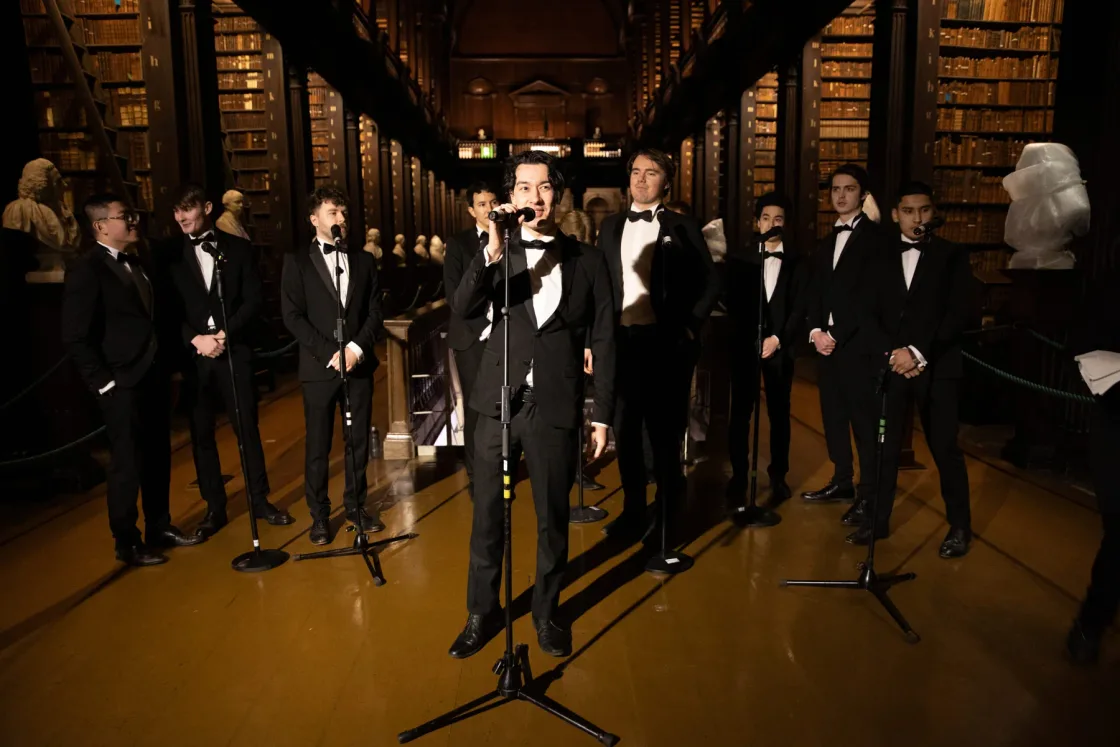 Singers performing between bookshelves in a vaulted library.