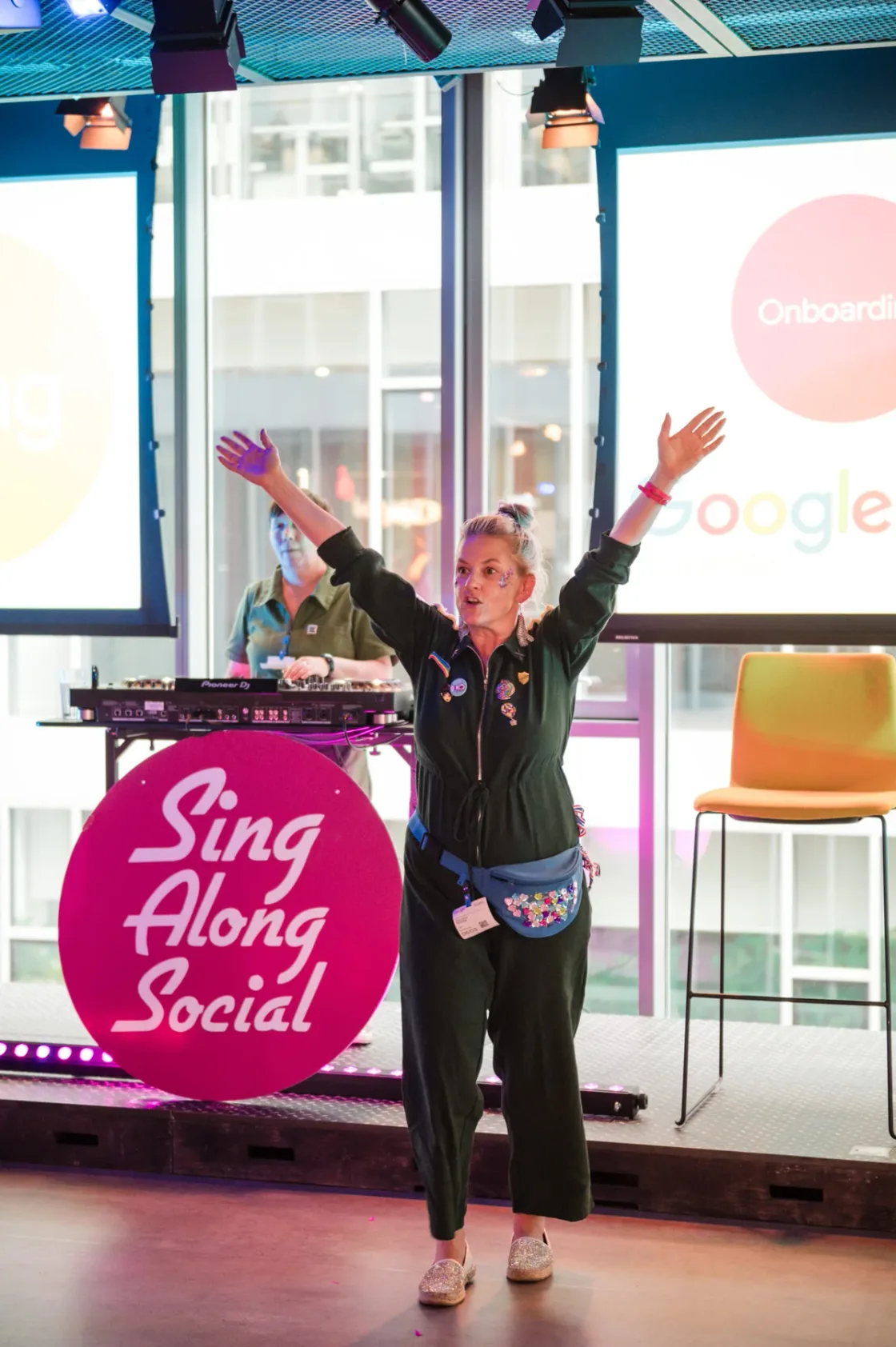 A performer raising their arms beside a Sing Along Social stand.