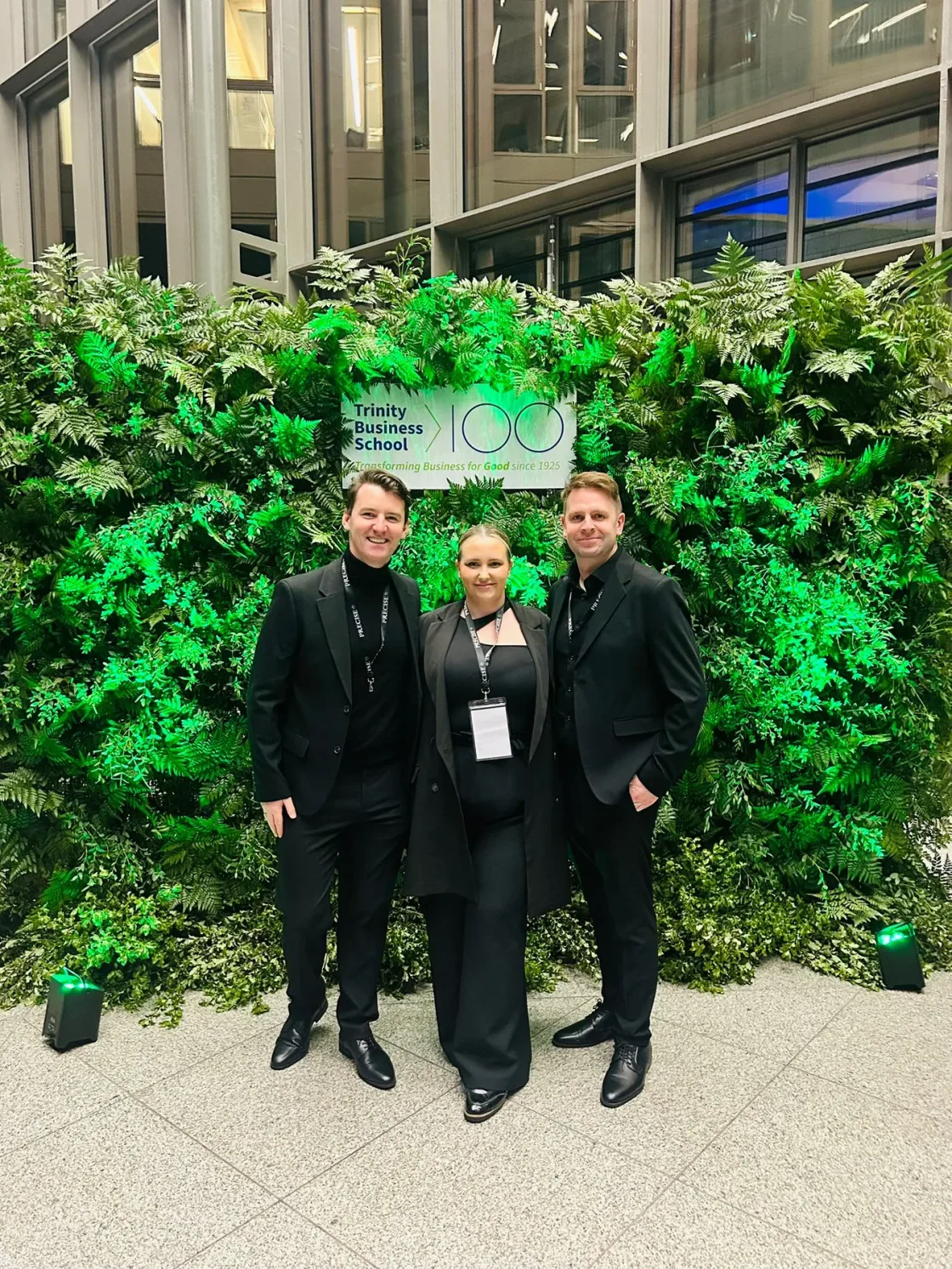 Three people posing in front of a green foliage display.