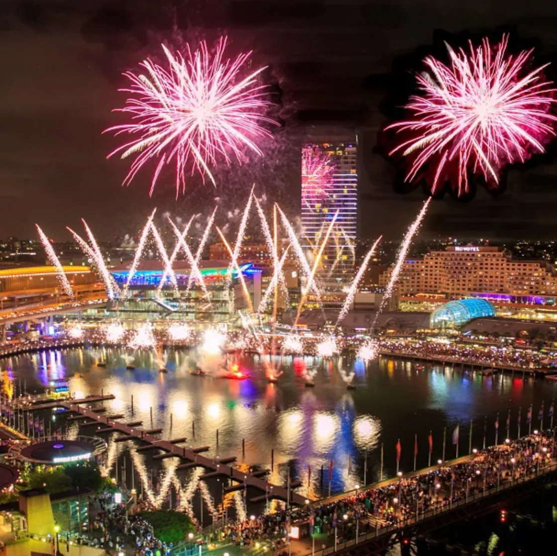 Pink fireworks above an illuminated riverside precinct.