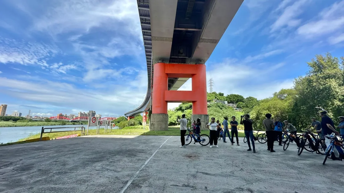 A group with bicycles gathered beneath a large bridge.