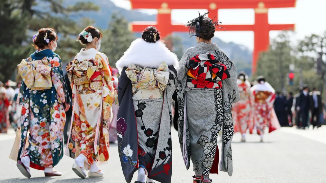 Visitors wearing patterned kimono walking towards a red torii gate.