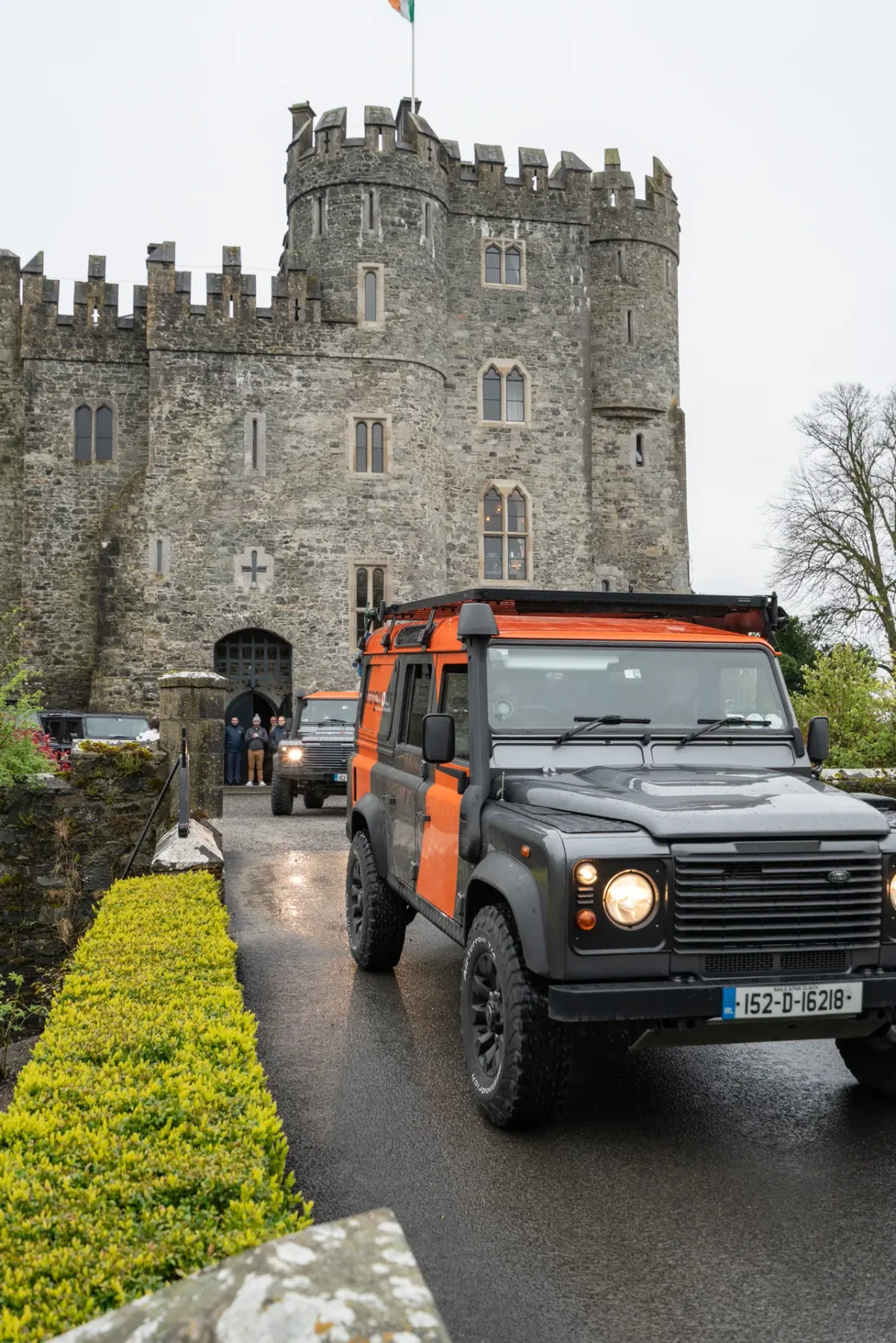 Land Rover vehicles parked outside the stone towers of a castle.