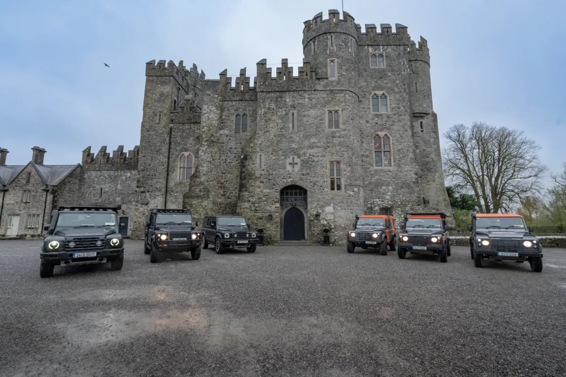 Land Rover vehicles arranged outside the stone towers of Kilkea Castle in Ireland.