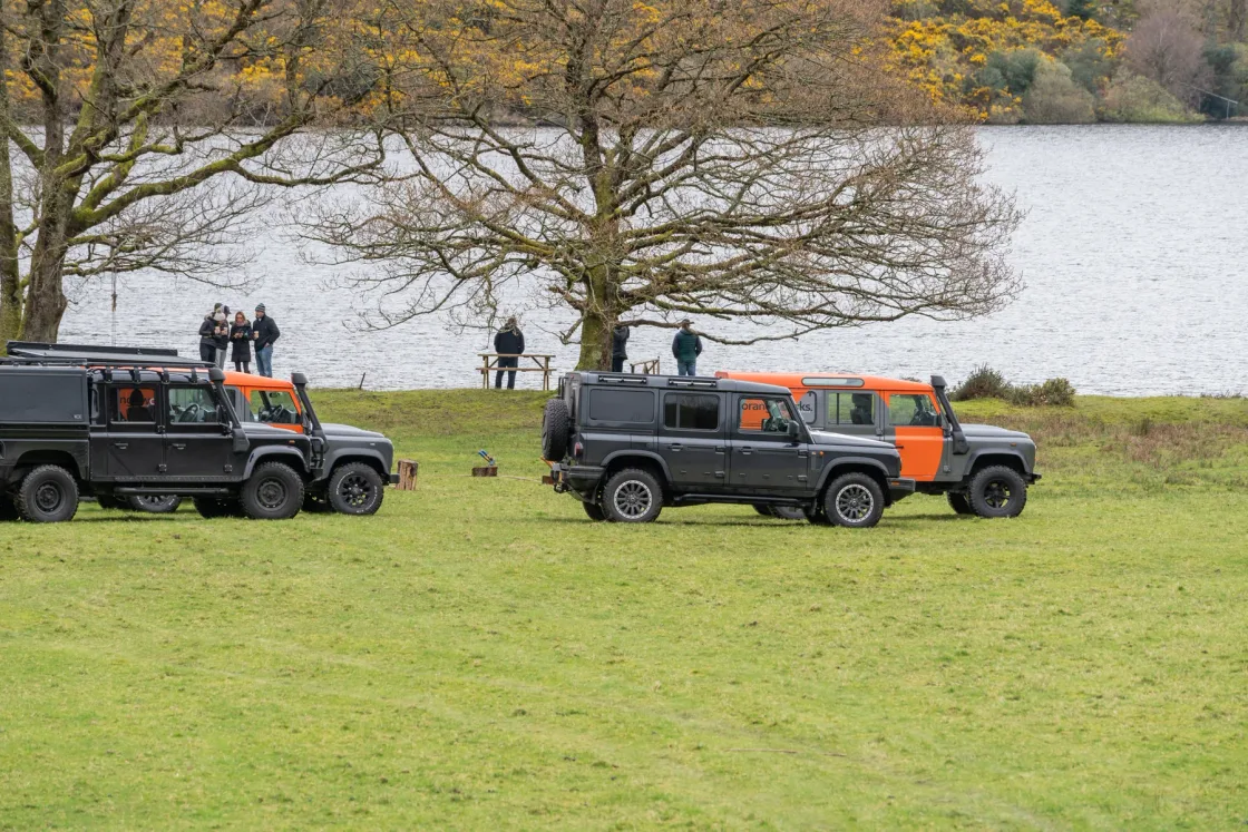 Land Rover vehicles parked beneath mature trees on a lawn.