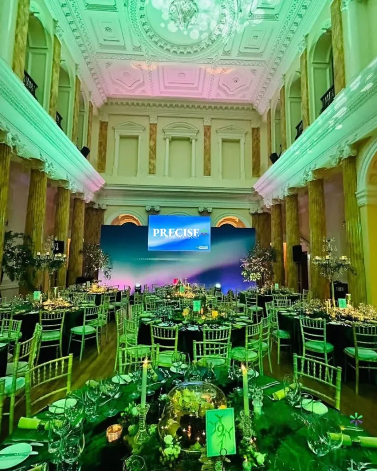 A grand dining hall illuminated in green with a presentation screen at the far end.