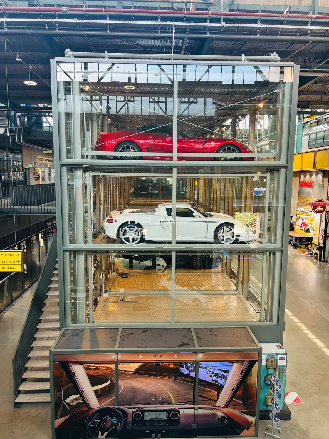 Cars displayed on stacked platforms inside a glass-and-steel structure.