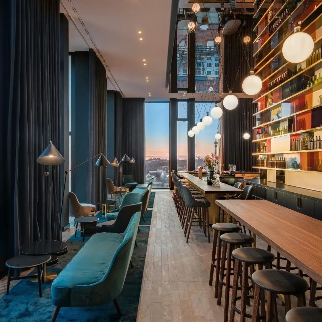 A long bar with turquoise seating, pendant lights and tall shelves.