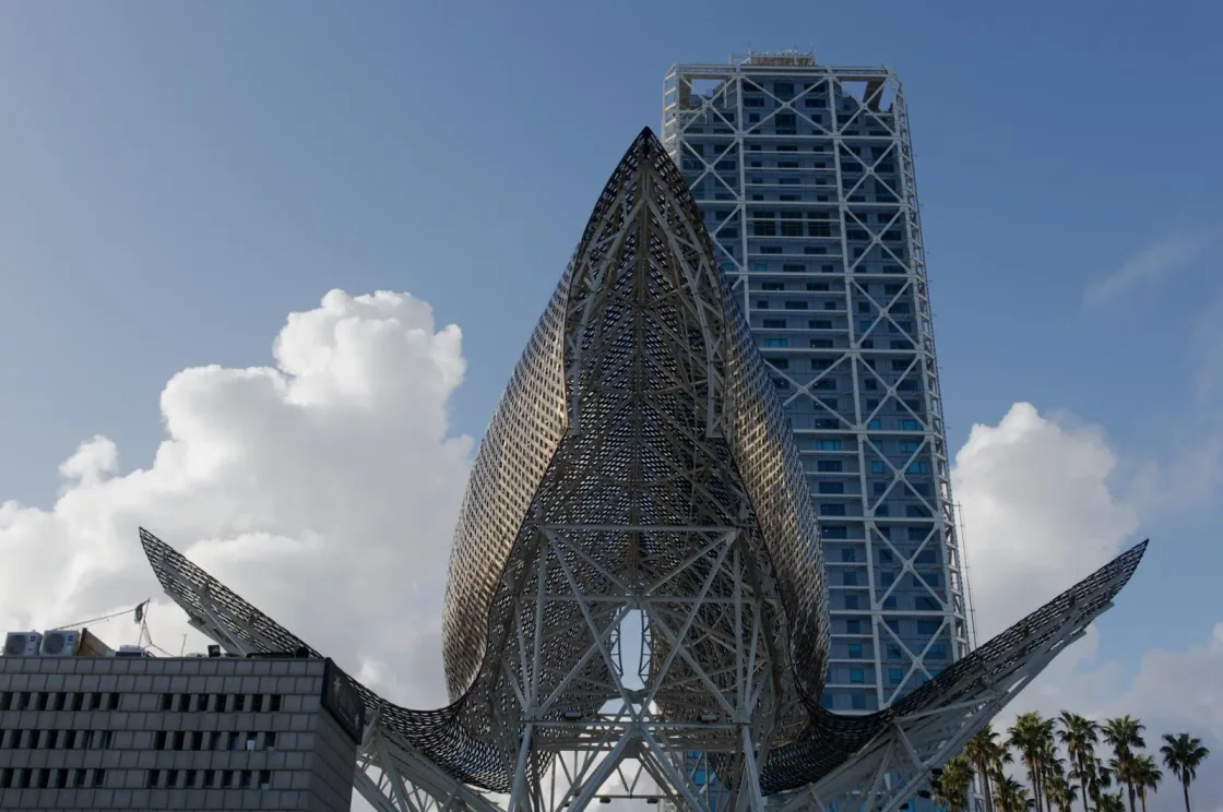 A curved metal sculpture beside a tall waterfront building.