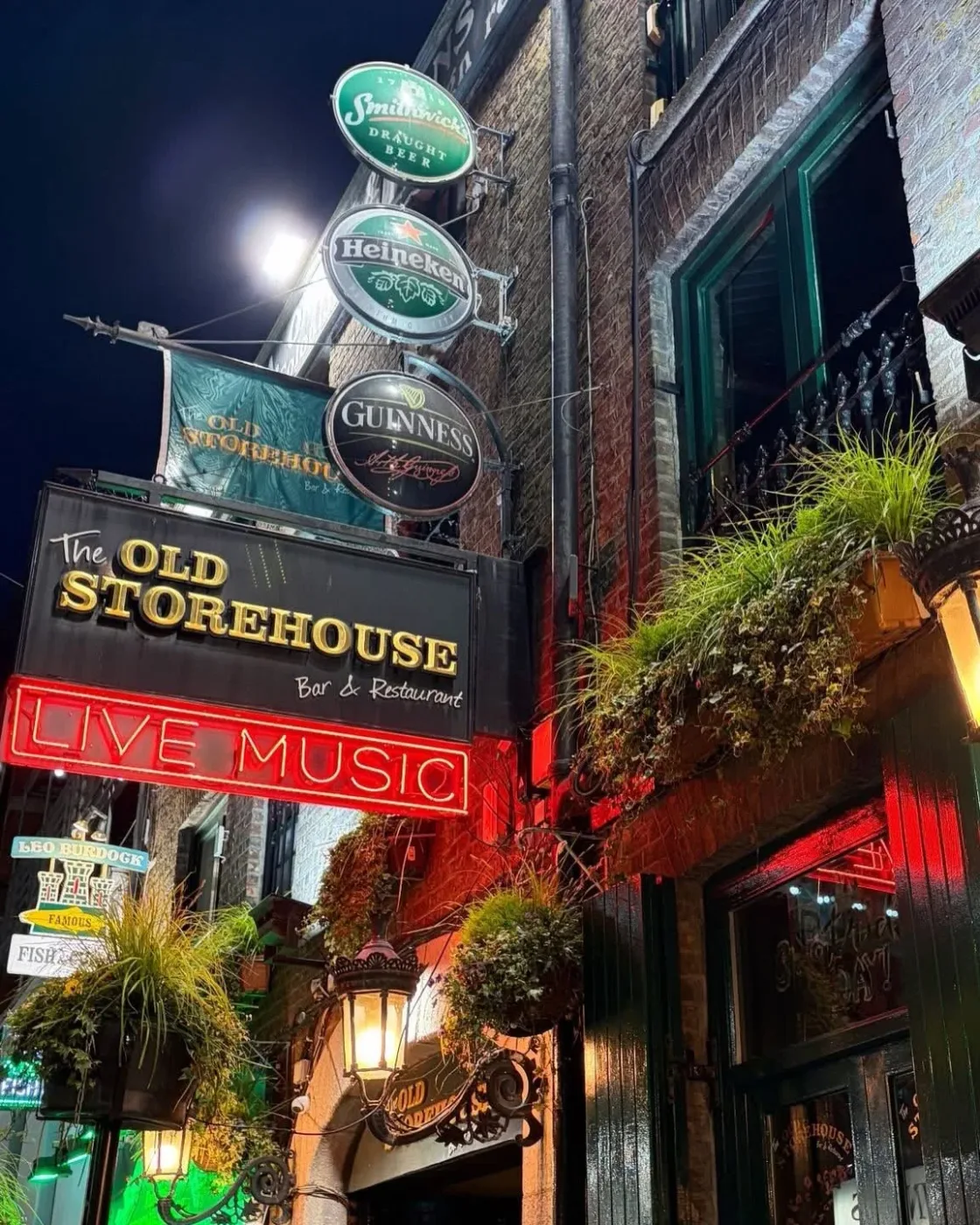 An illuminated Old Storehouse pub sign above a busy street entrance.