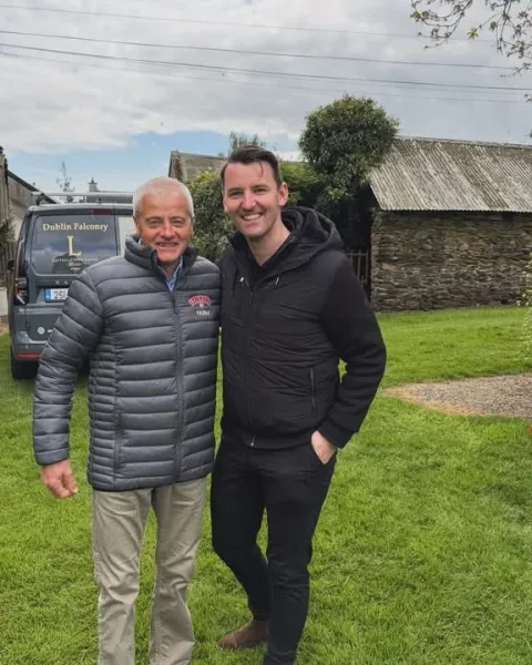 Two people posing together outside stone farm buildings.