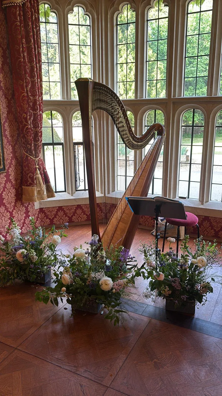 A harp placed beside tall windows and a low floral arrangement.