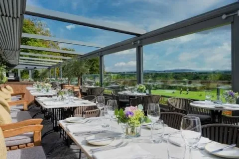 Dining tables beside large windows overlooking gardens and countryside.