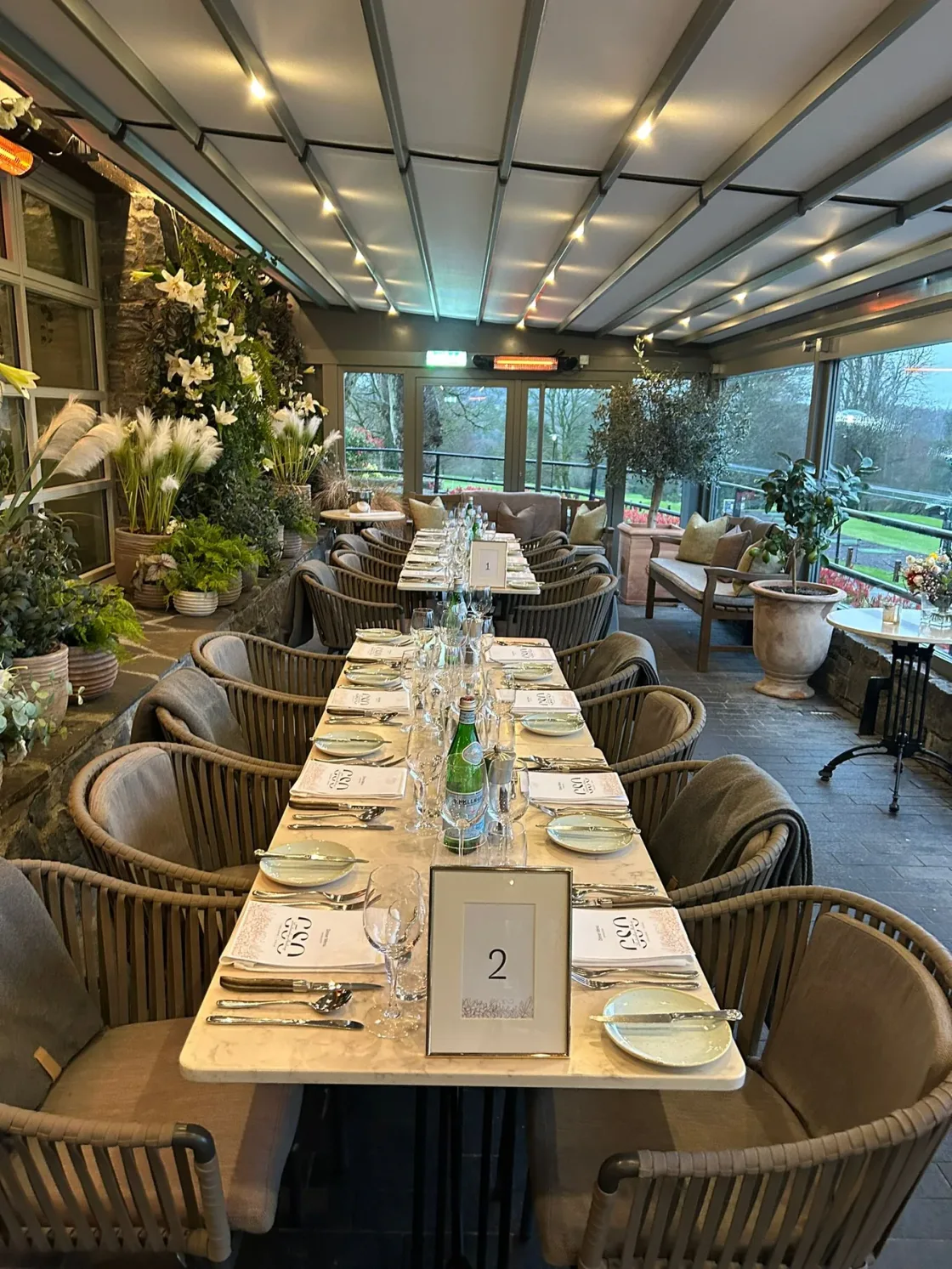 A long dining table set beneath ceiling beams and glass lighting fixtures.