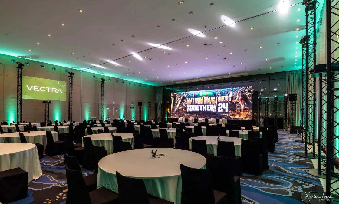 Conference tables facing a presentation stage in a room lit in green.