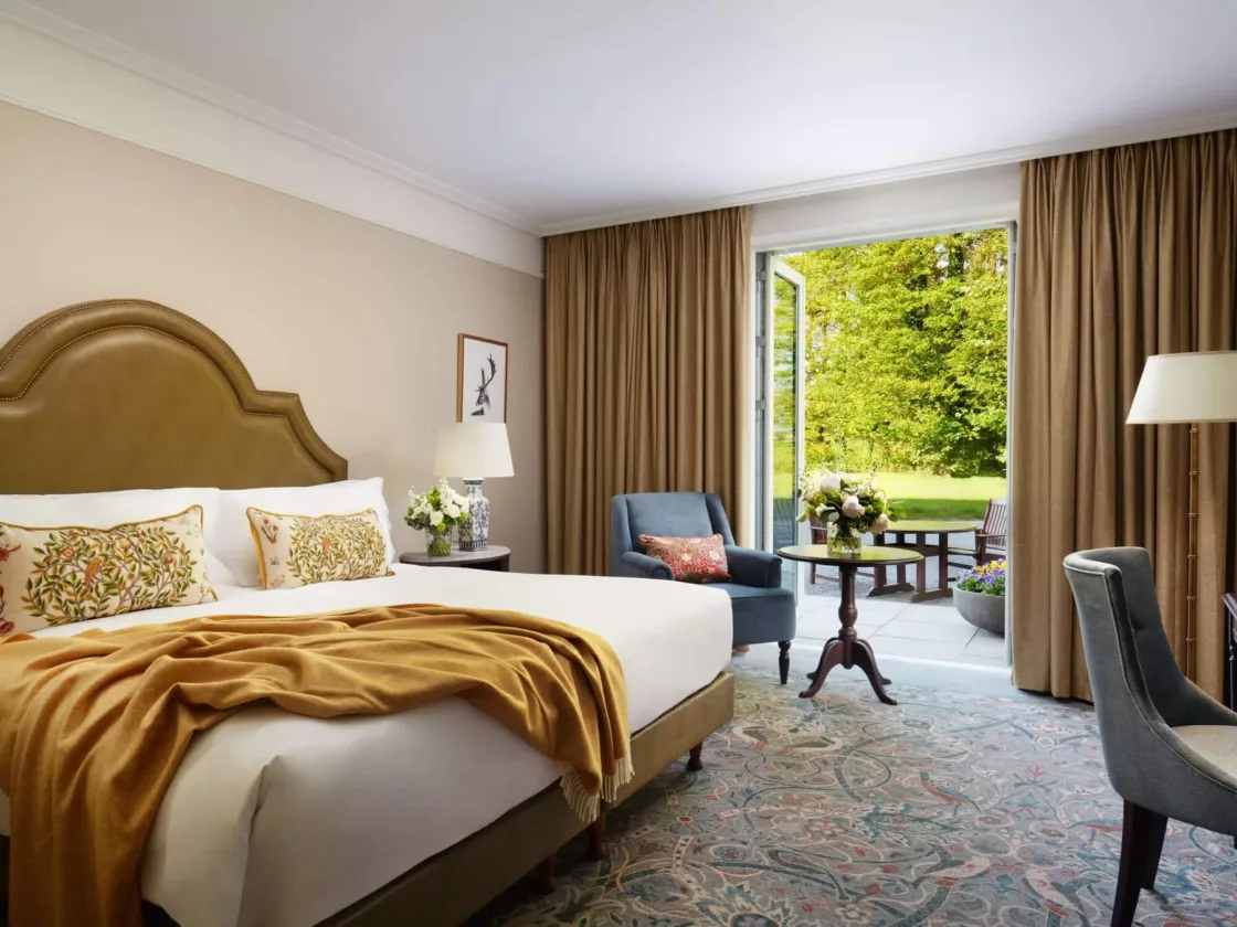 A guest bedroom with gold accents and a view of trees outside.