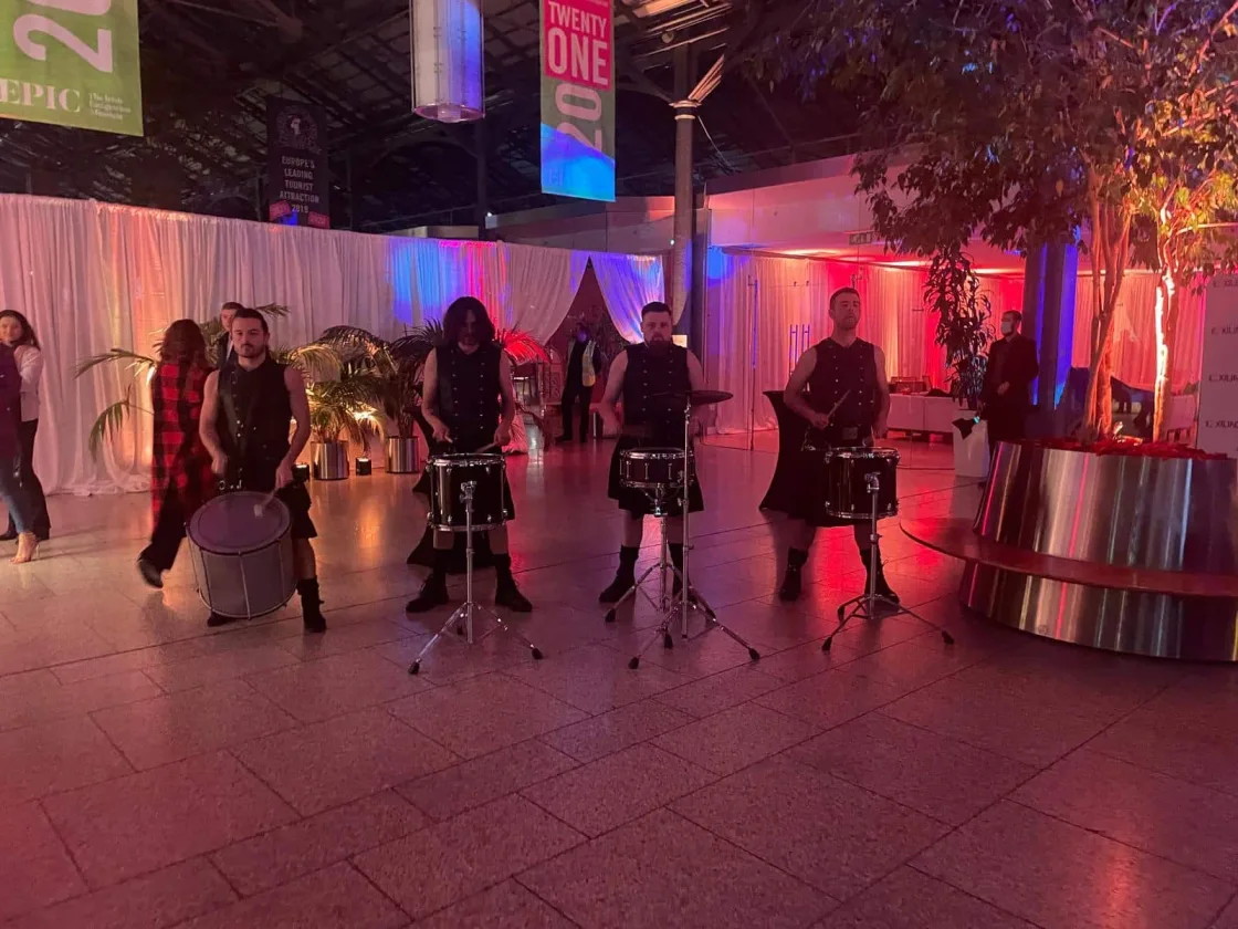 Bagpipers performing in a venue lit in pink and purple.