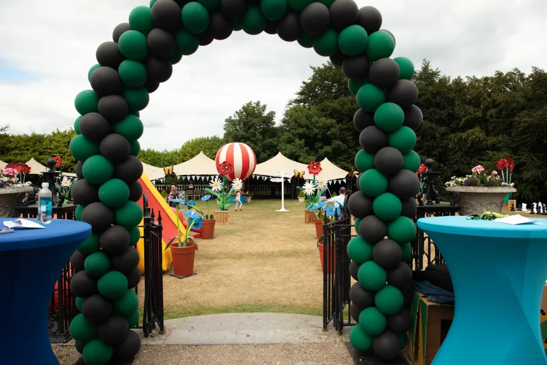 A green-and-black balloon arch at the entrance to an outdoor celebration.