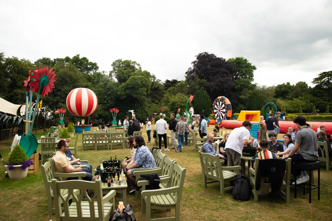 Guests seated at lawn tables among colourful outdoor event decorations.