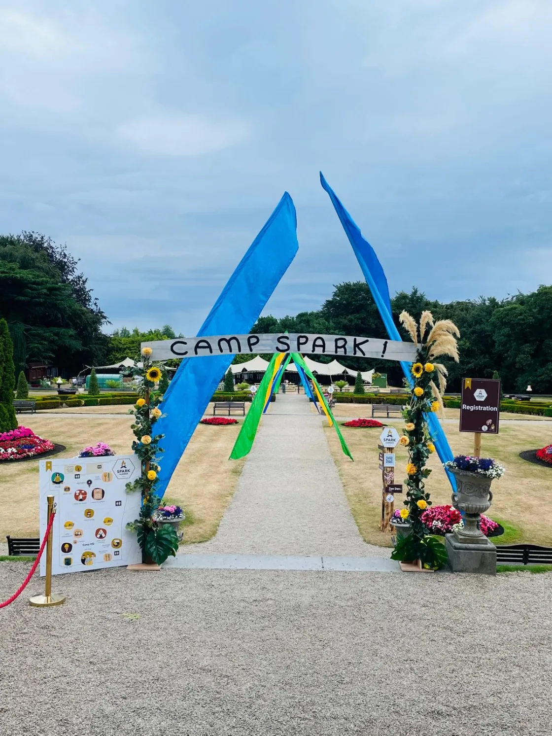 A blue-and-green outdoor event entrance framed by colourful flowers.