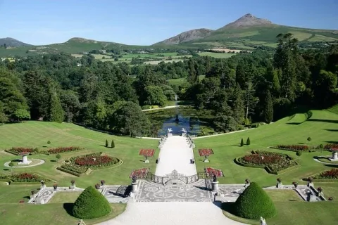 Formal gardens and a tree-lined valley viewed from a stone terrace.