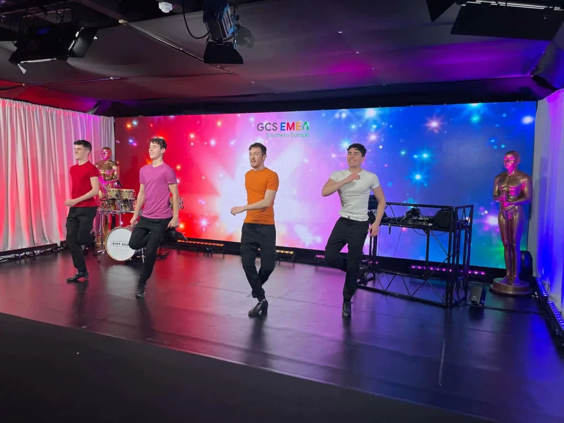 Dancers performing on an indoor stage in front of a colourful backdrop.