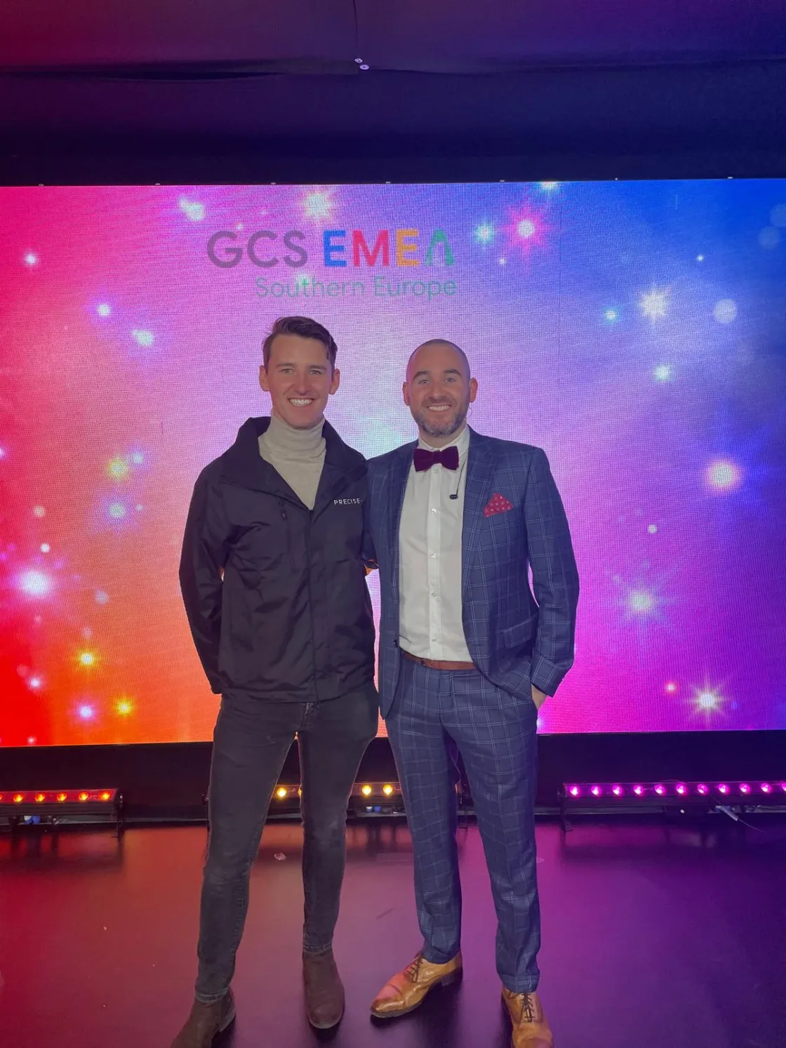 Two guests posing in front of a colourful event backdrop.