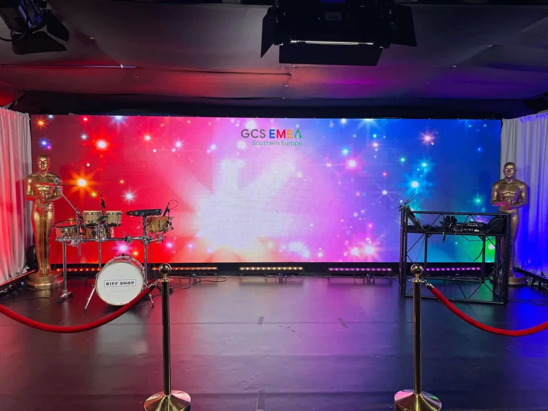 A stage prepared with drums, microphones and a colourful illuminated backdrop.