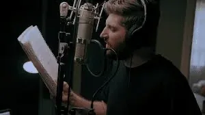 A person wearing headphones reading into a studio microphone.