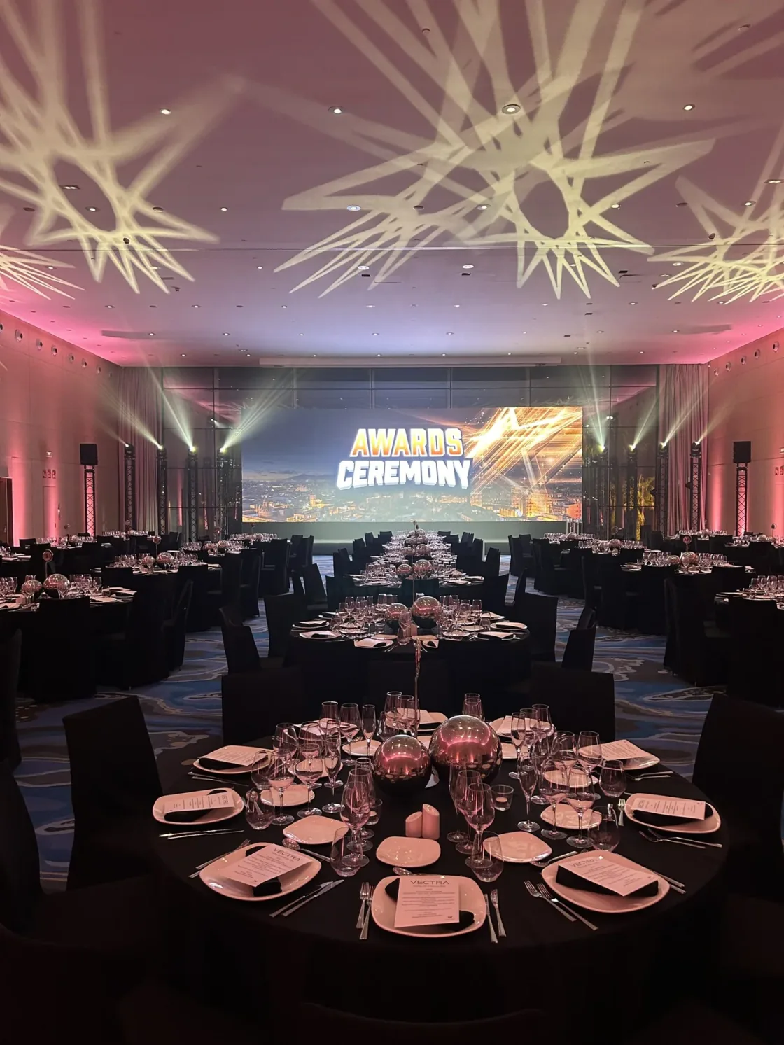 Dinner tables facing a presentation screen beneath star-shaped ceiling projections.
