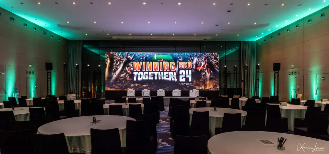 Round conference tables facing a stage in a room lit in green.