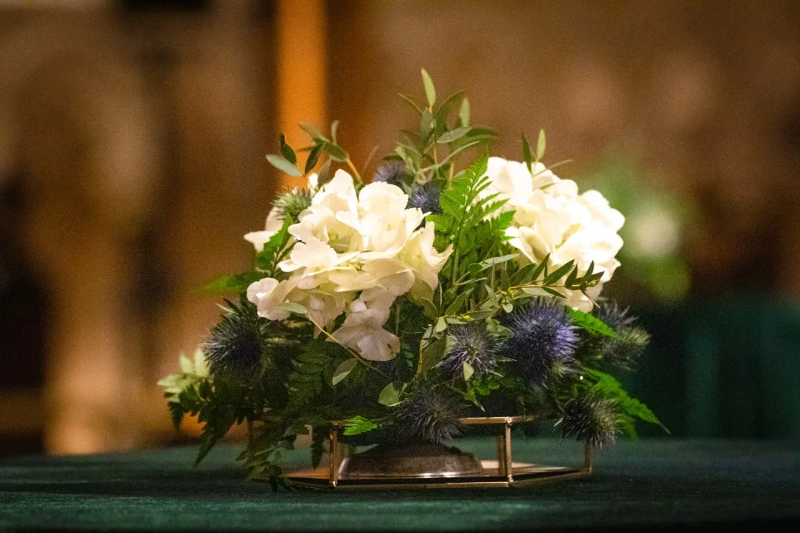 A low centrepiece of white flowers and green foliage on a dark dining table.