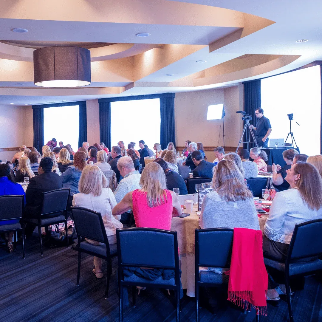 Delegates seated around round tables during a conference presentation.