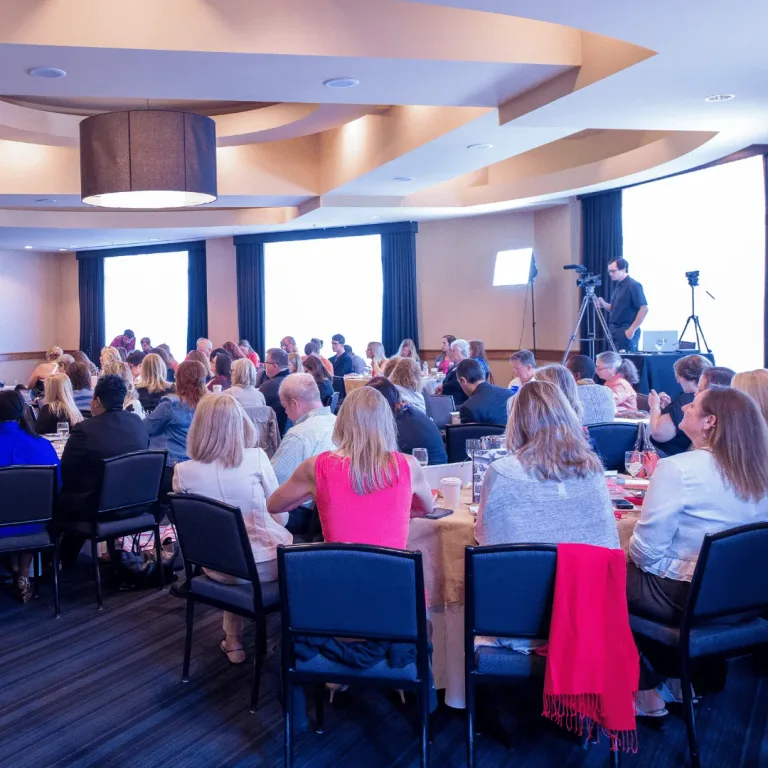Delegates seated around round tables during a conference presentation.