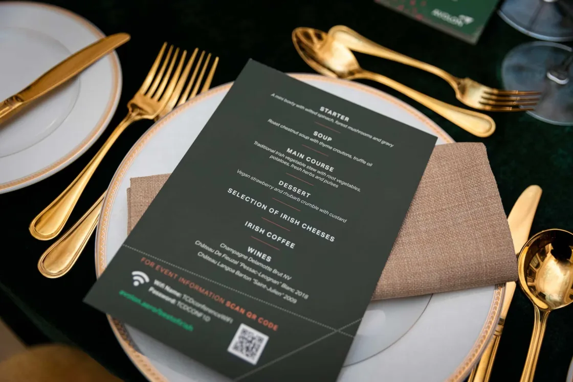 A printed menu on a white plate beside gold-coloured cutlery.