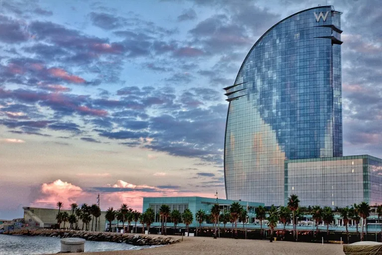 A curved glass hotel tower beside the waterfront at sunset.